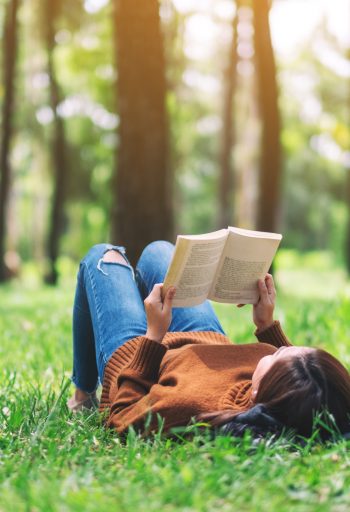 A beautiful Asian woman lying and reading a book in the park