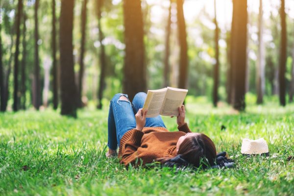 A beautiful Asian woman lying and reading a book in the park