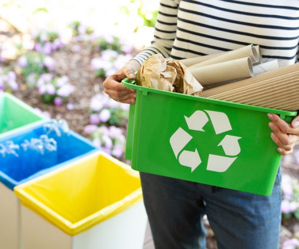 Close-up of a green basket with a recycling symbol with papers held by a woman